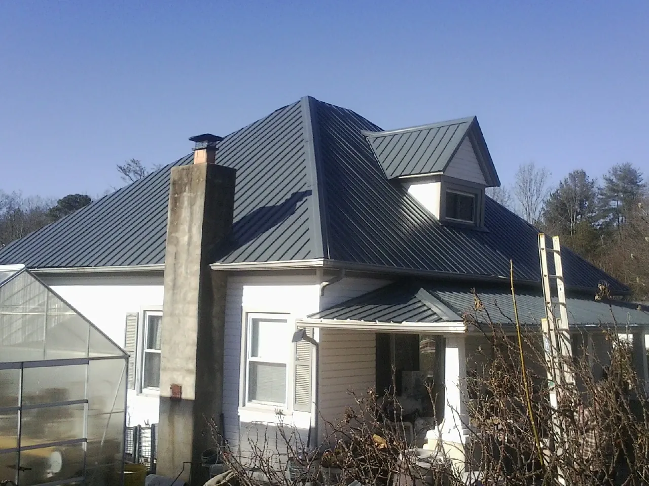 Dark blue standing seam metal roof on a white farmhouse with dormer — Slate & Tile Roof Repair by Roofing Brothers in Lone Tree