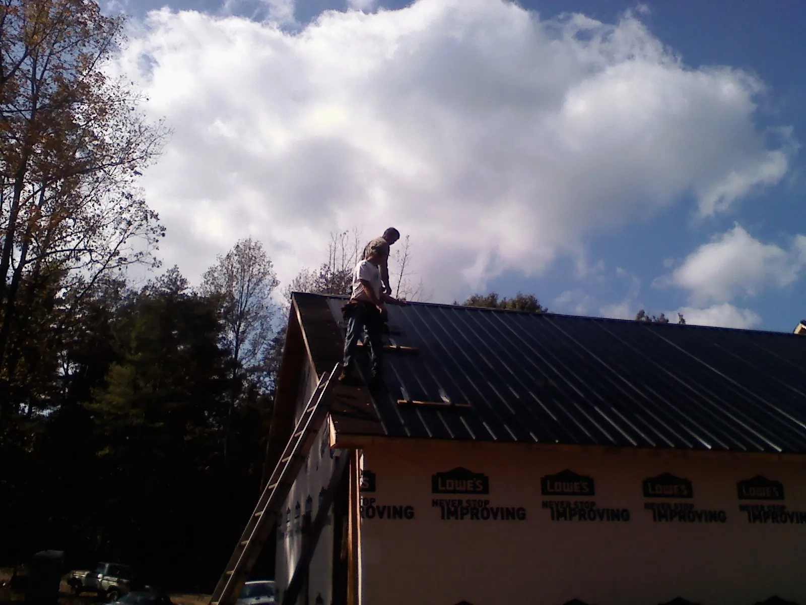 Roofer fastening dark metal panels high against a cloudy sky, from a Roof Inspection job in Lone Tree